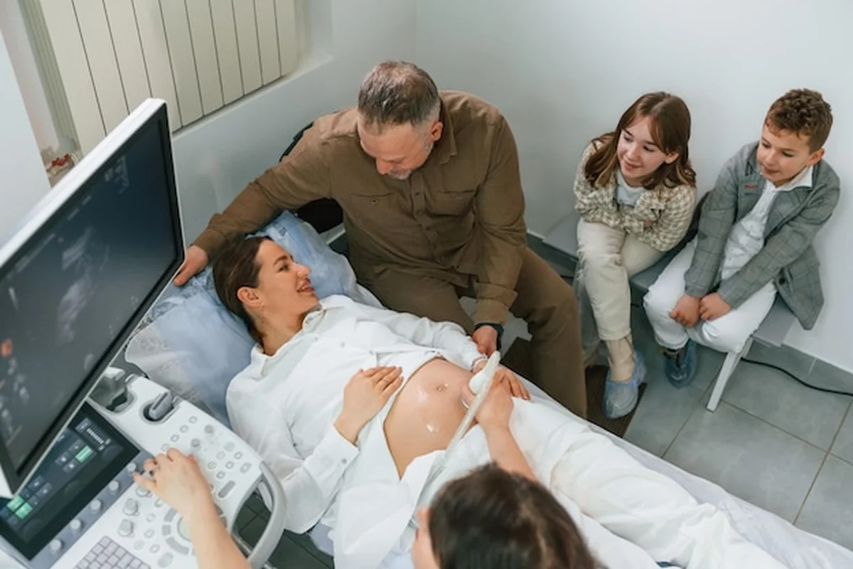 Kobieta w ciąży leżąca na łóżku szpitalnym, mąż i dzieci przy niej, lekarz wykonuje ultradźwięki