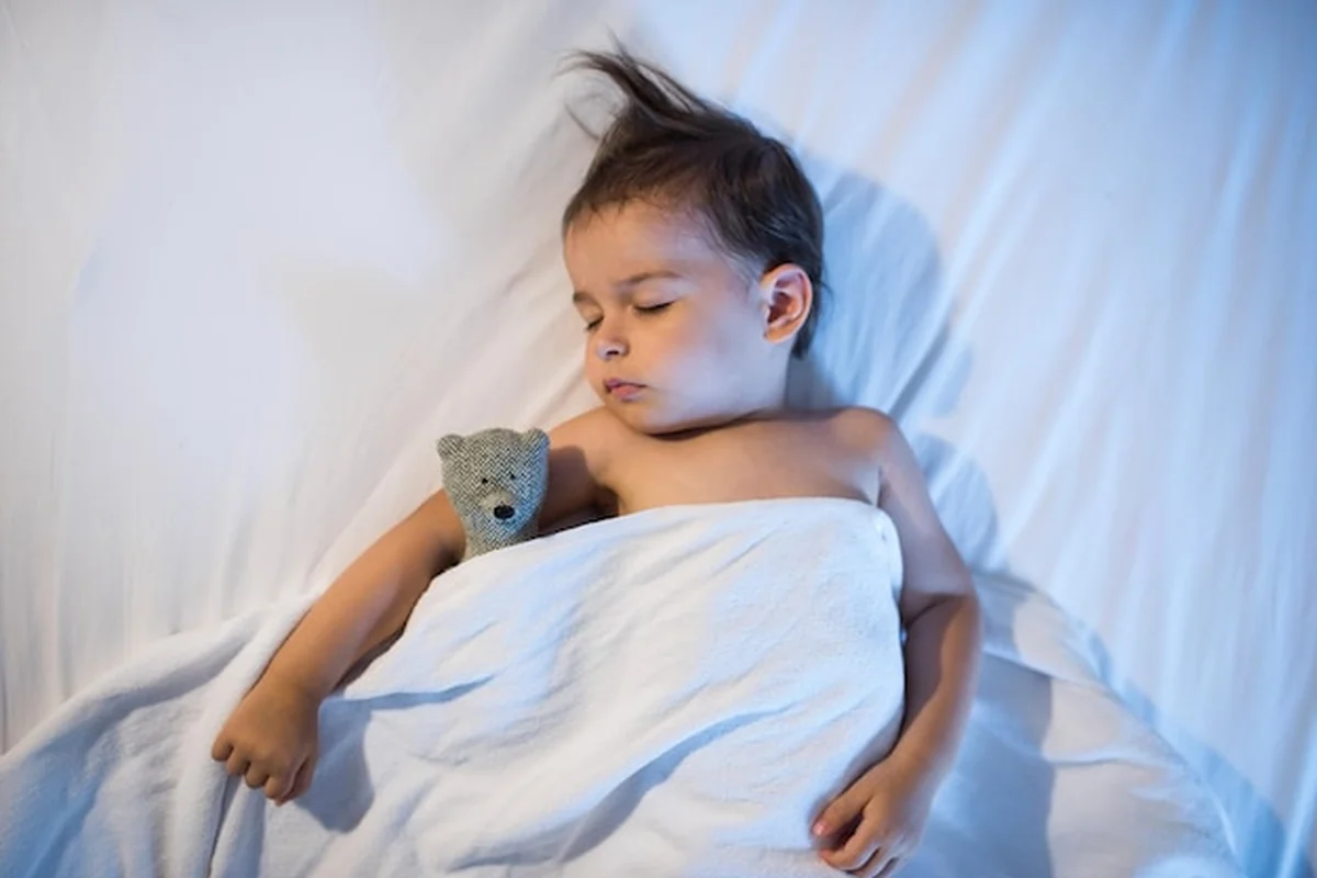 Malutkie dziecko śpiące w białym łóżku z lampą i misiem-zabawką