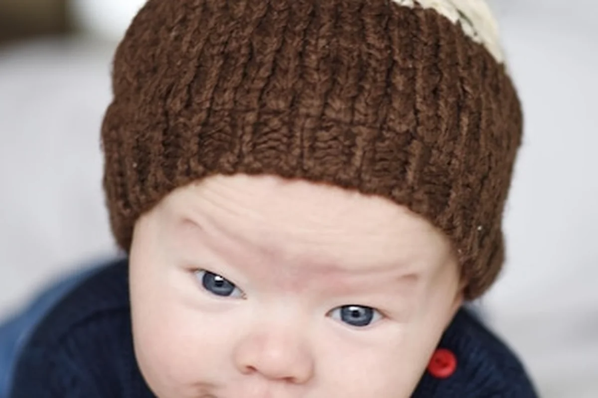 Noworodek w wełnianej czapce i swetrze leżący na brzuszku