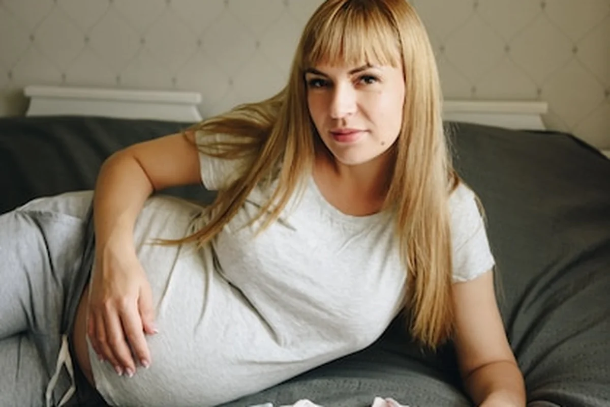 Ciężarna blondynka w żółtym T-shirt leżąca na łóżku