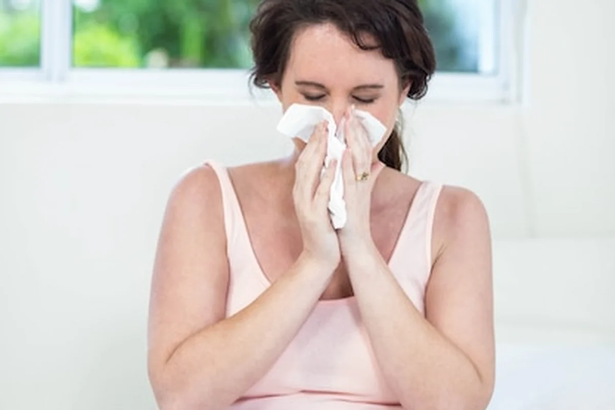 Kobieta w ciąży siedzi na łóżku kichając