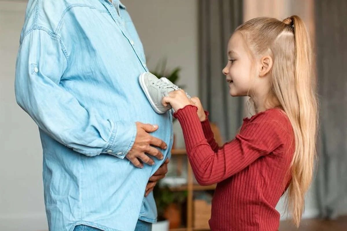 Dziewczynka kładzie buciki na brzuchu ciężarnej mamy podczas zabawy