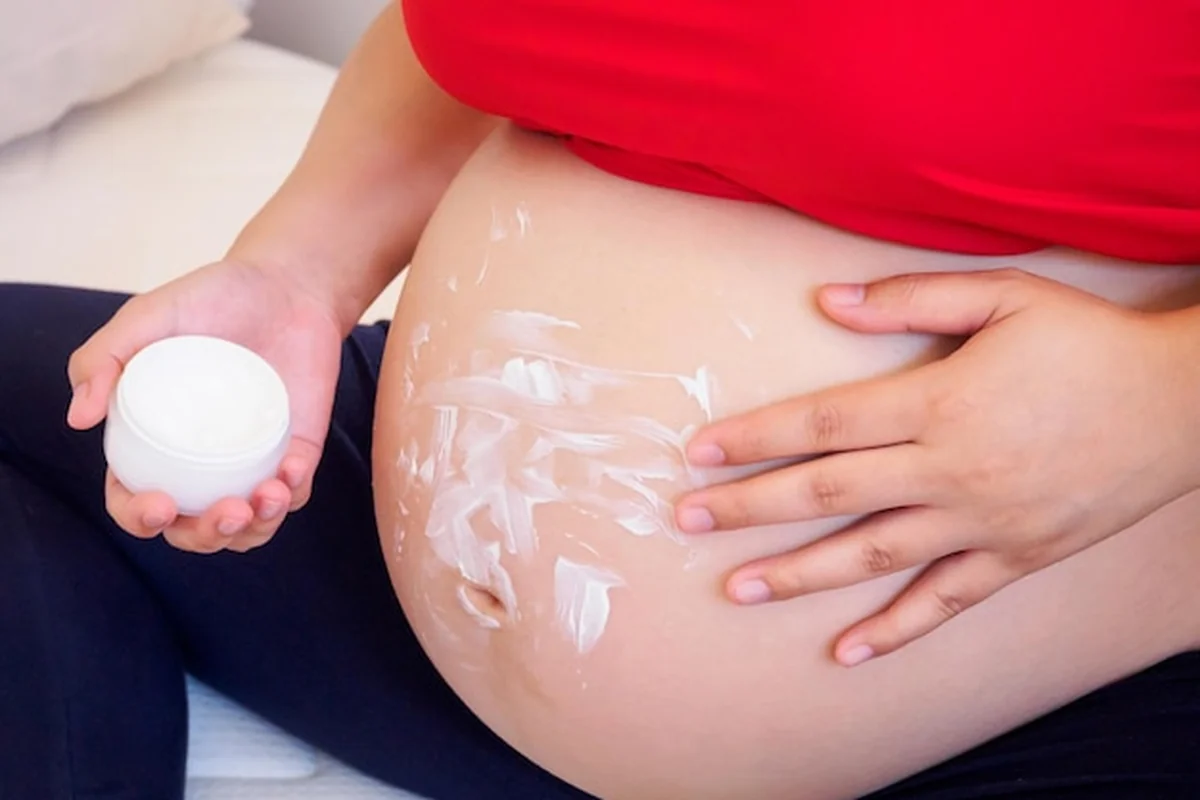 Kobieta w ciąży nakładająca krem na rozstępy na brzuchu