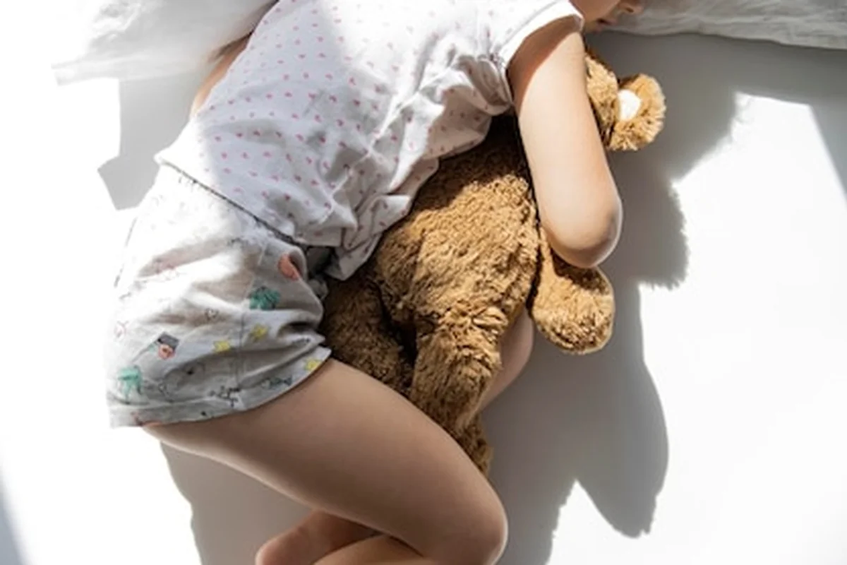 Dziewczynka śpi z pluszowym misiem na białym łóżku